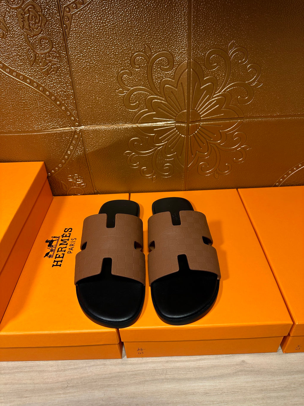 Tan leather slide sandal with black rubber sole and signature H-style strap