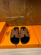Tan leather slide sandal with black rubber sole and signature H-style strap