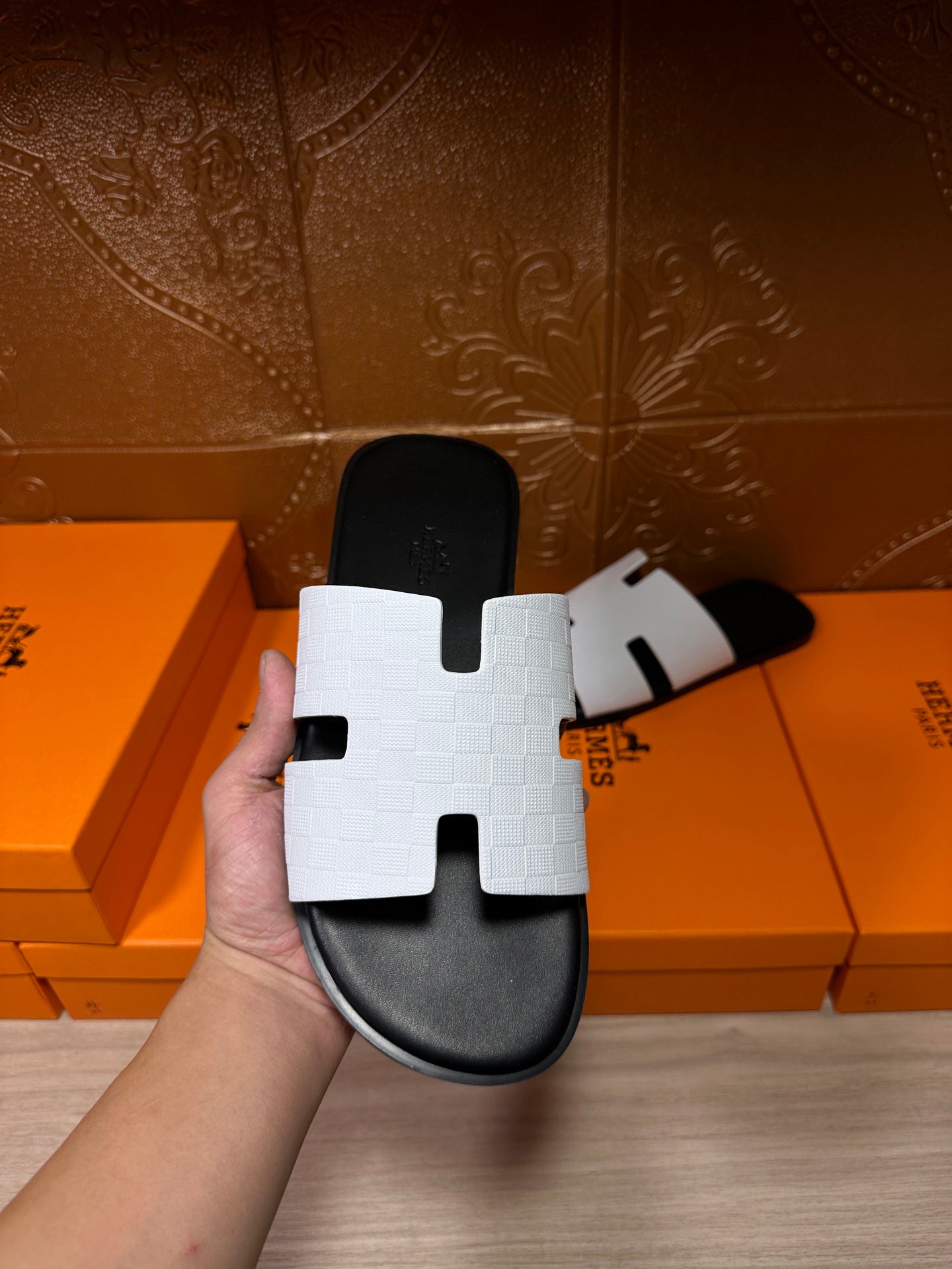 Hermes slide sandal held up, white strap with H-cutout over black sole