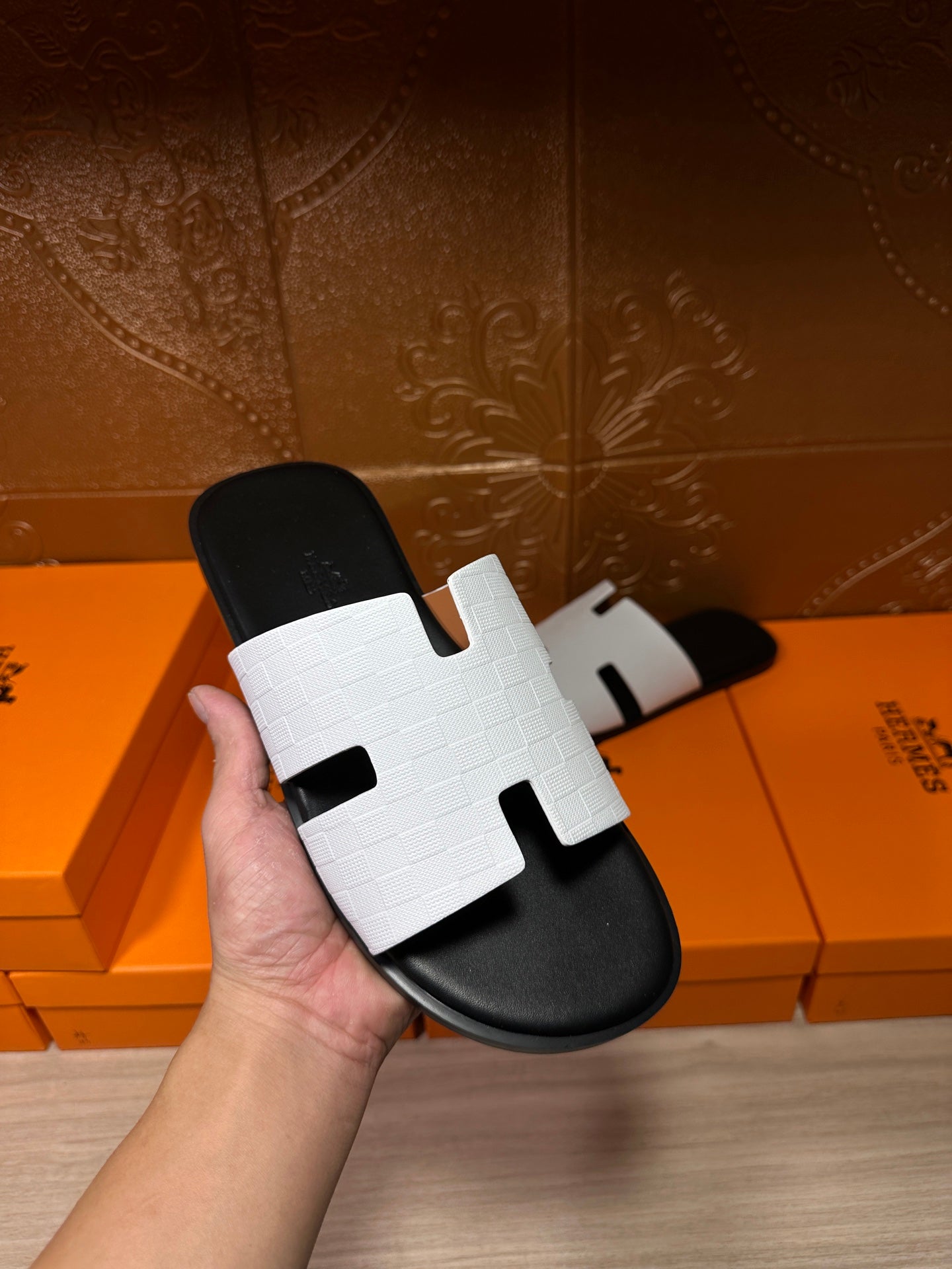 Hermes slide sandal held in hand, white textured strap over black footbed