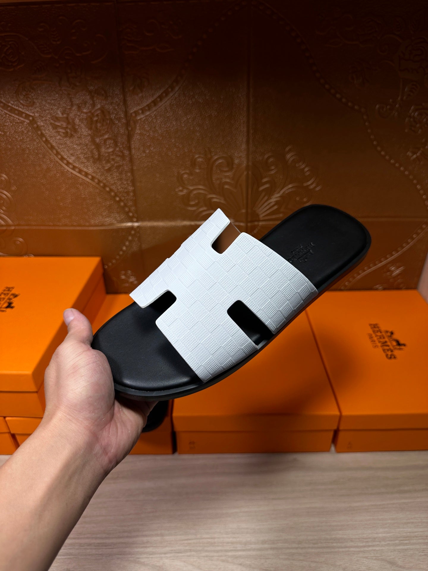 Hermes slide sandal held in hand, white H-cutout strap on black footbed