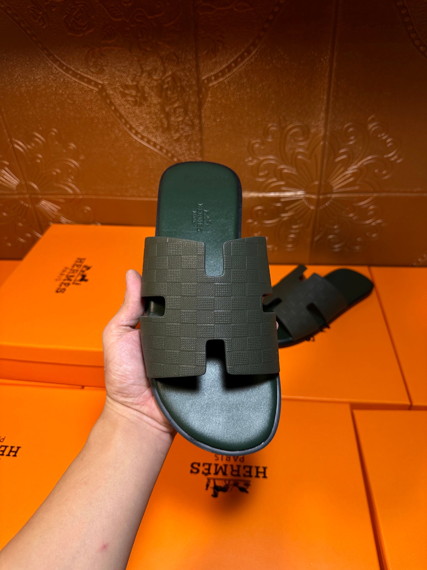 Hermes slide sandal held by sole, dark green footbed with H-style strap