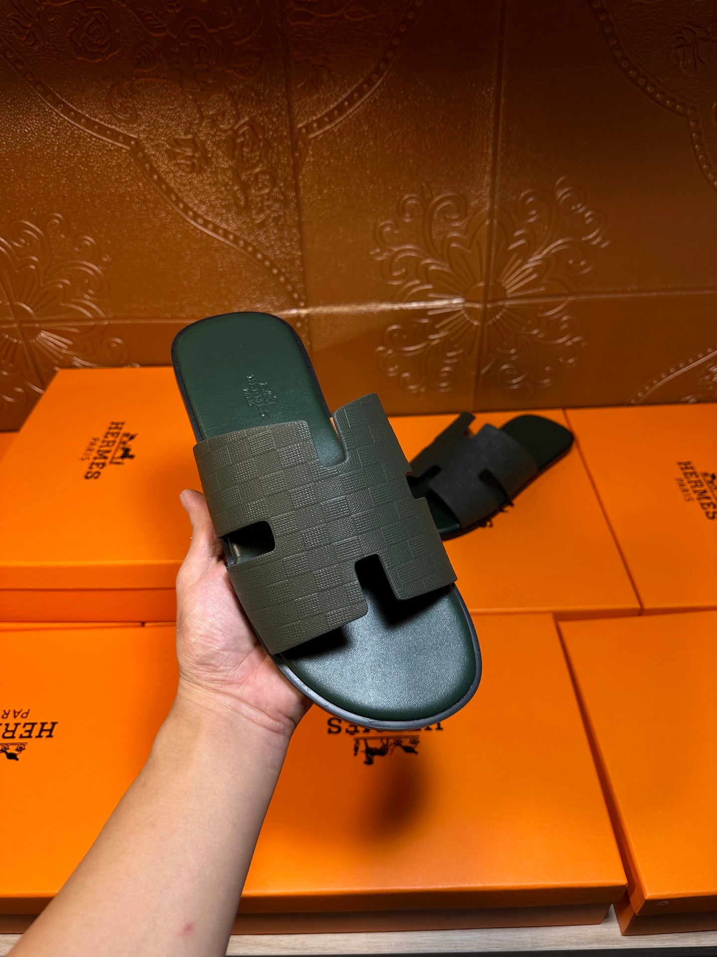 Hermes slide sandal held in hand, dark green wide H-style strap with open toe