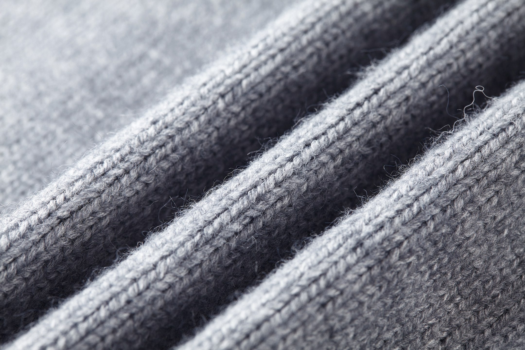 Close-up of gray knit fabric texture and ribbed trim on sweater.