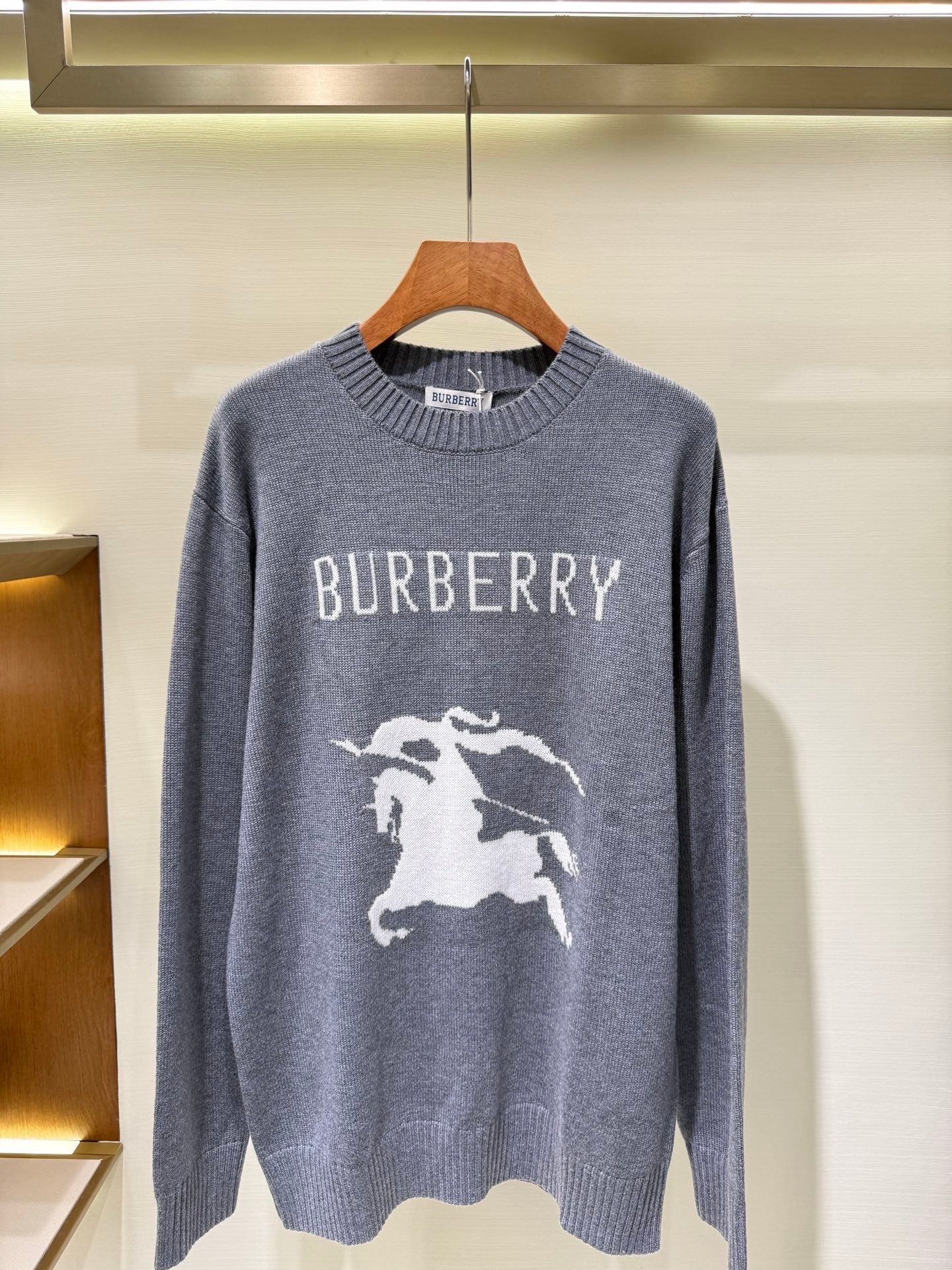 Gray knit sweater with “BURBERRY” lettering and white horse graphic on front.