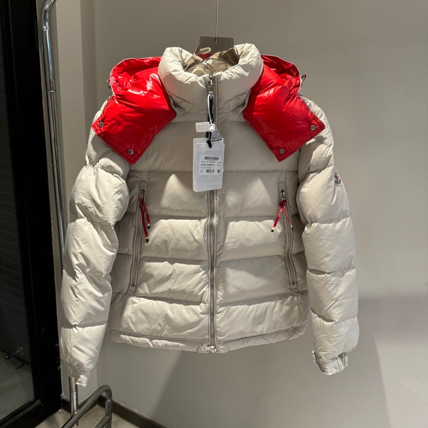 Long white puffer jacket with red hood lining, zip front, and quilted panels