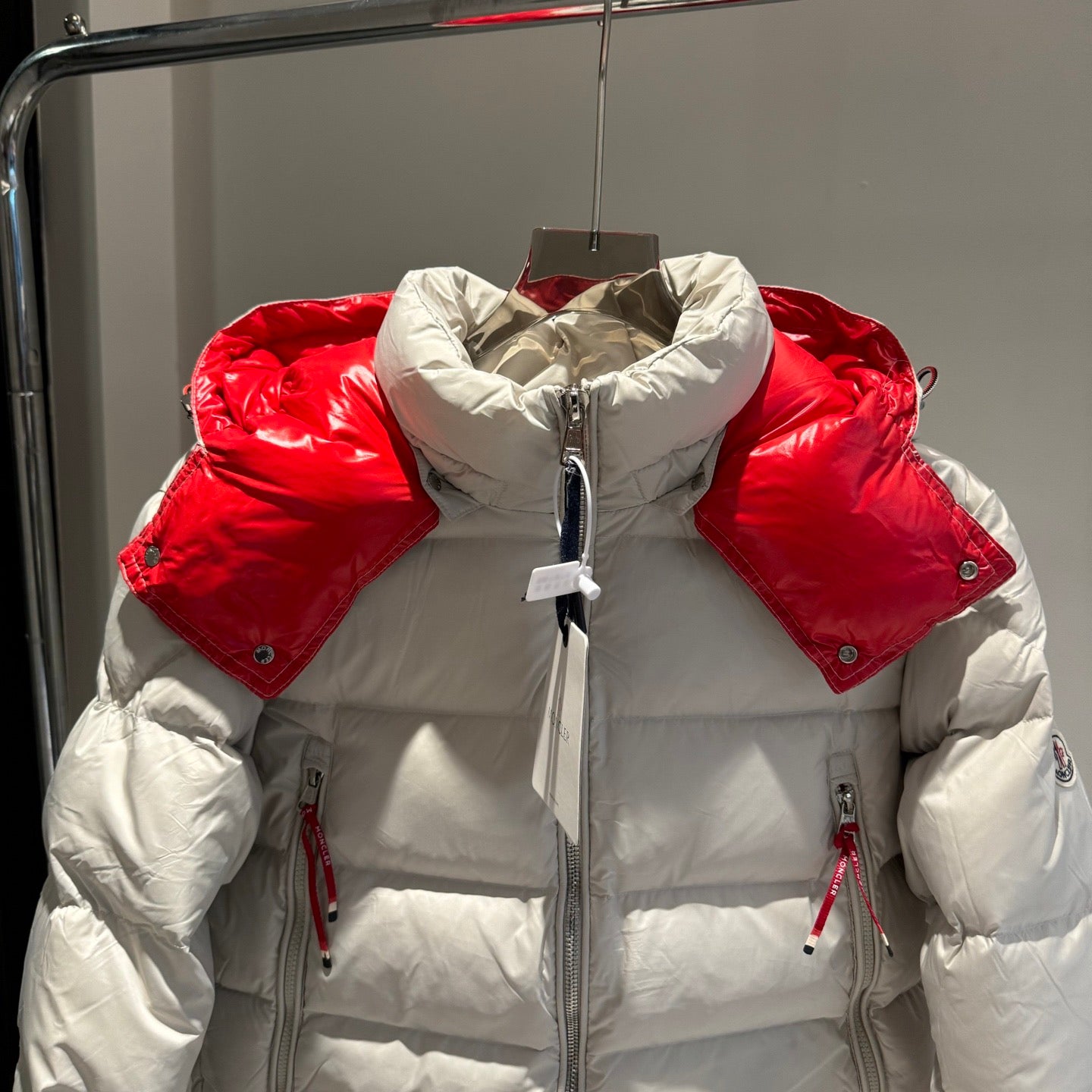 Long white puffer jacket with red collar, full-zip front, drawcord hood, and side zips