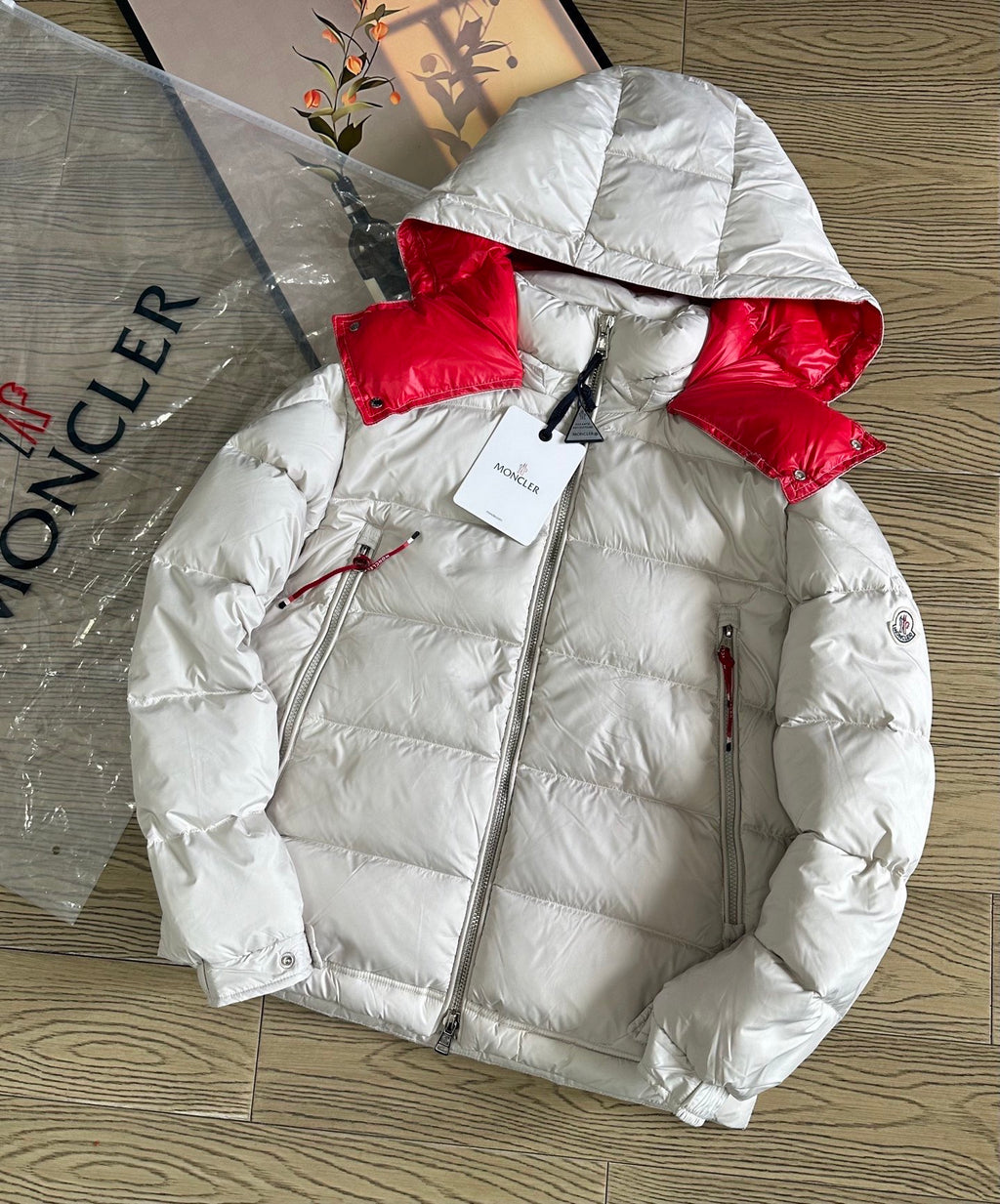 Long puffer jacket laid flat, white quilted fabric with red hood and zip front