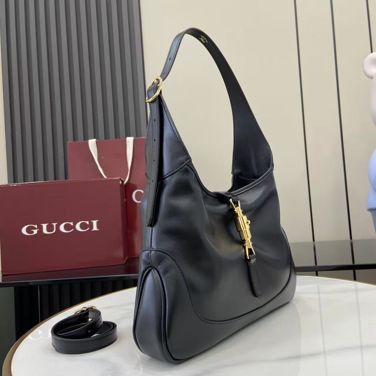 Black leather hobo bag, side view with shoulder strap and gold-tone front clasp