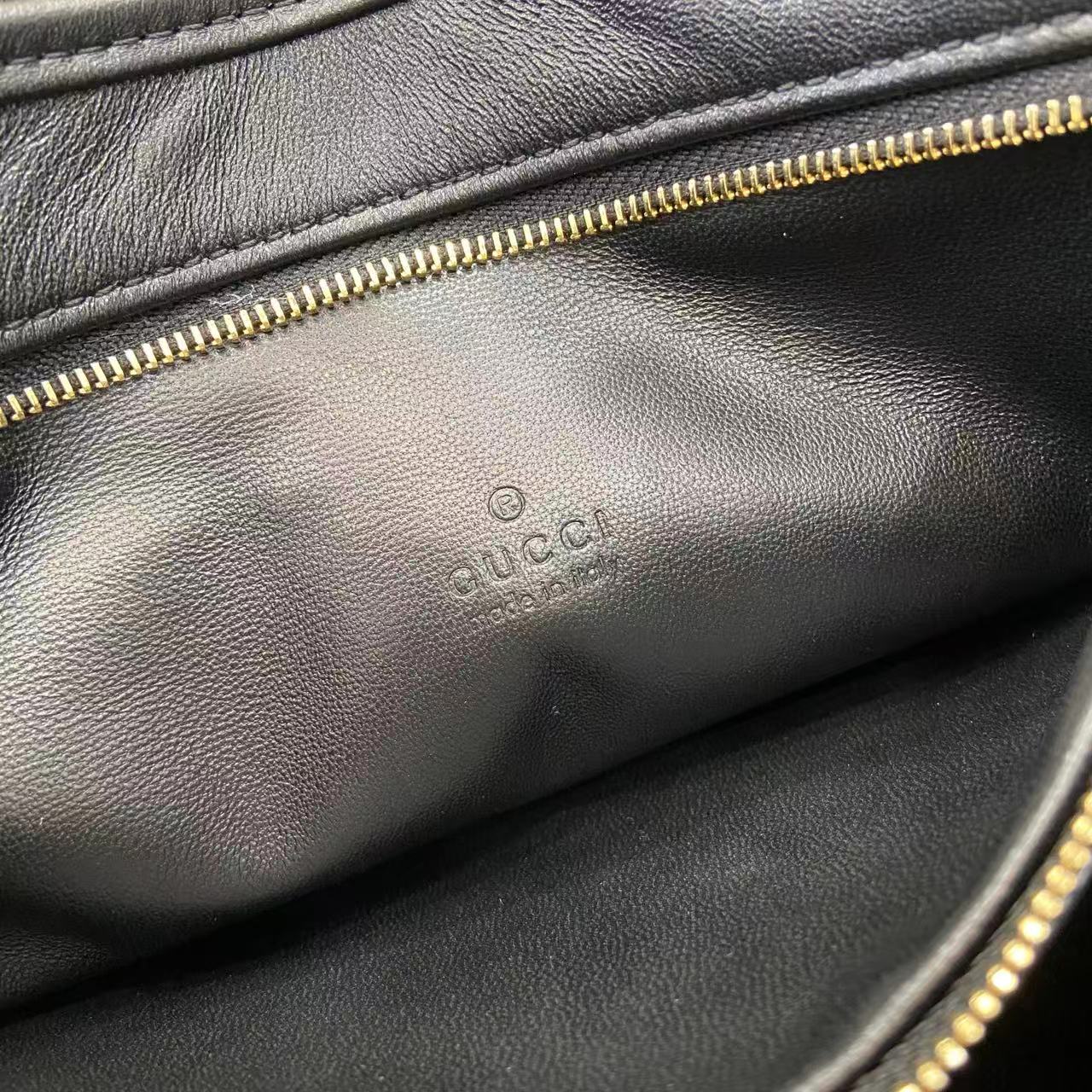 Black leather hobo bag close-up showing gold-tone zipper and stamped logo
