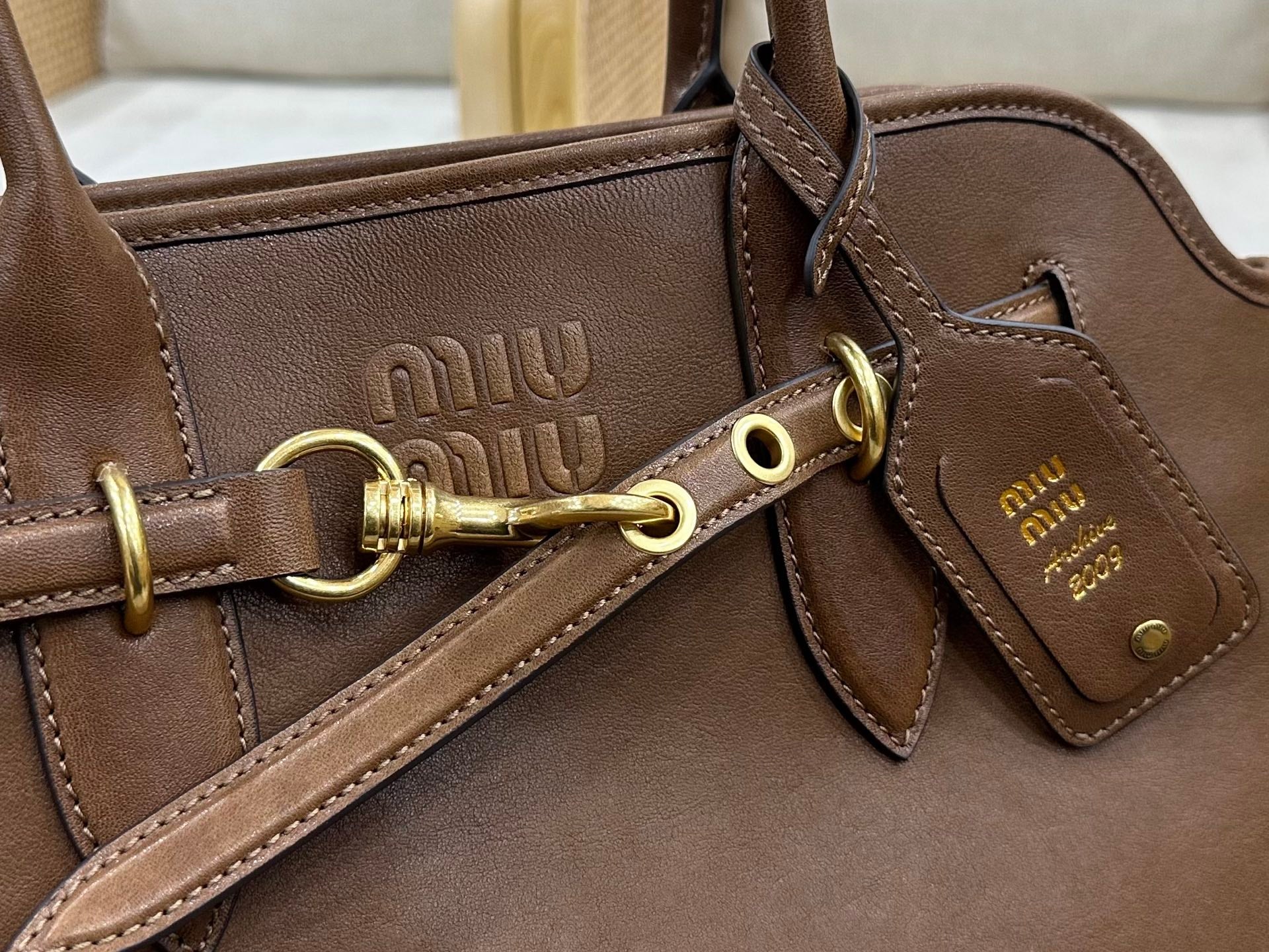 Brown leather handbag close-up of Miu Miu logo plate and clasp hardware