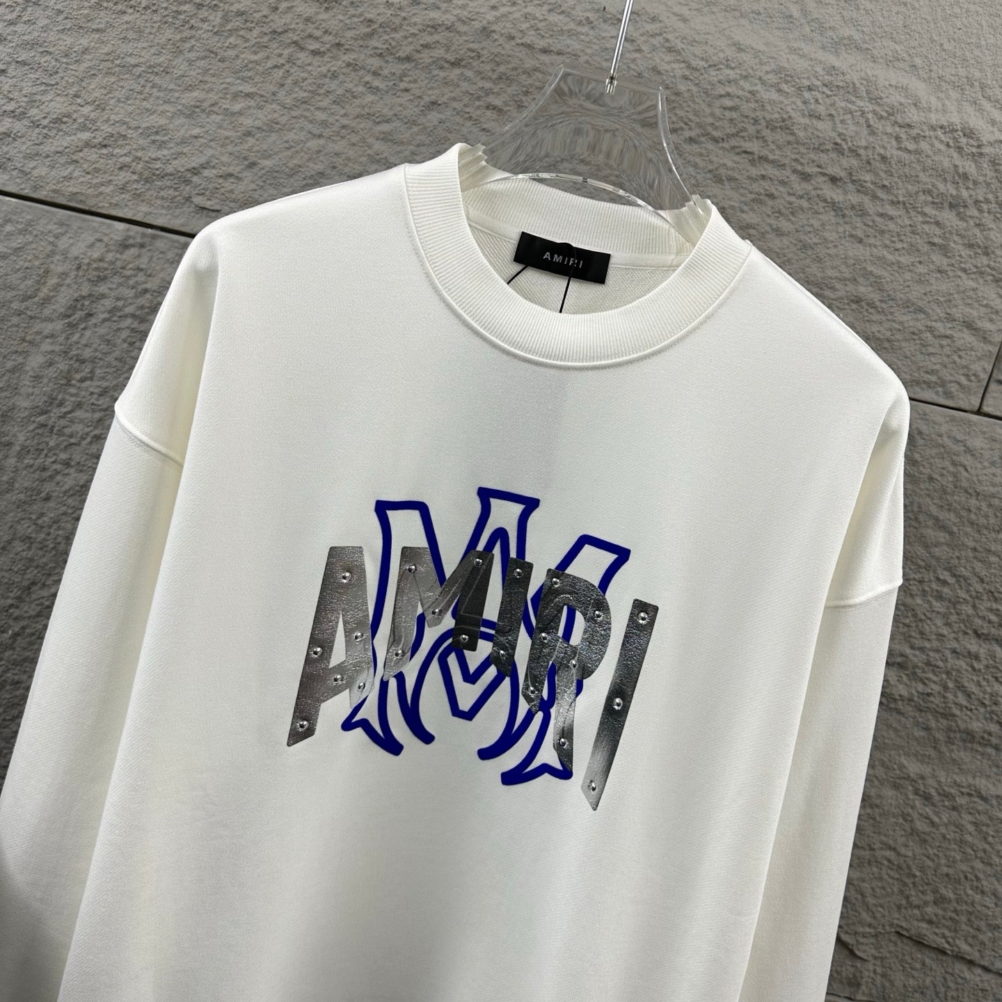White Amiri crewneck sweatshirt with blue graphic lettering and silver metallic panels