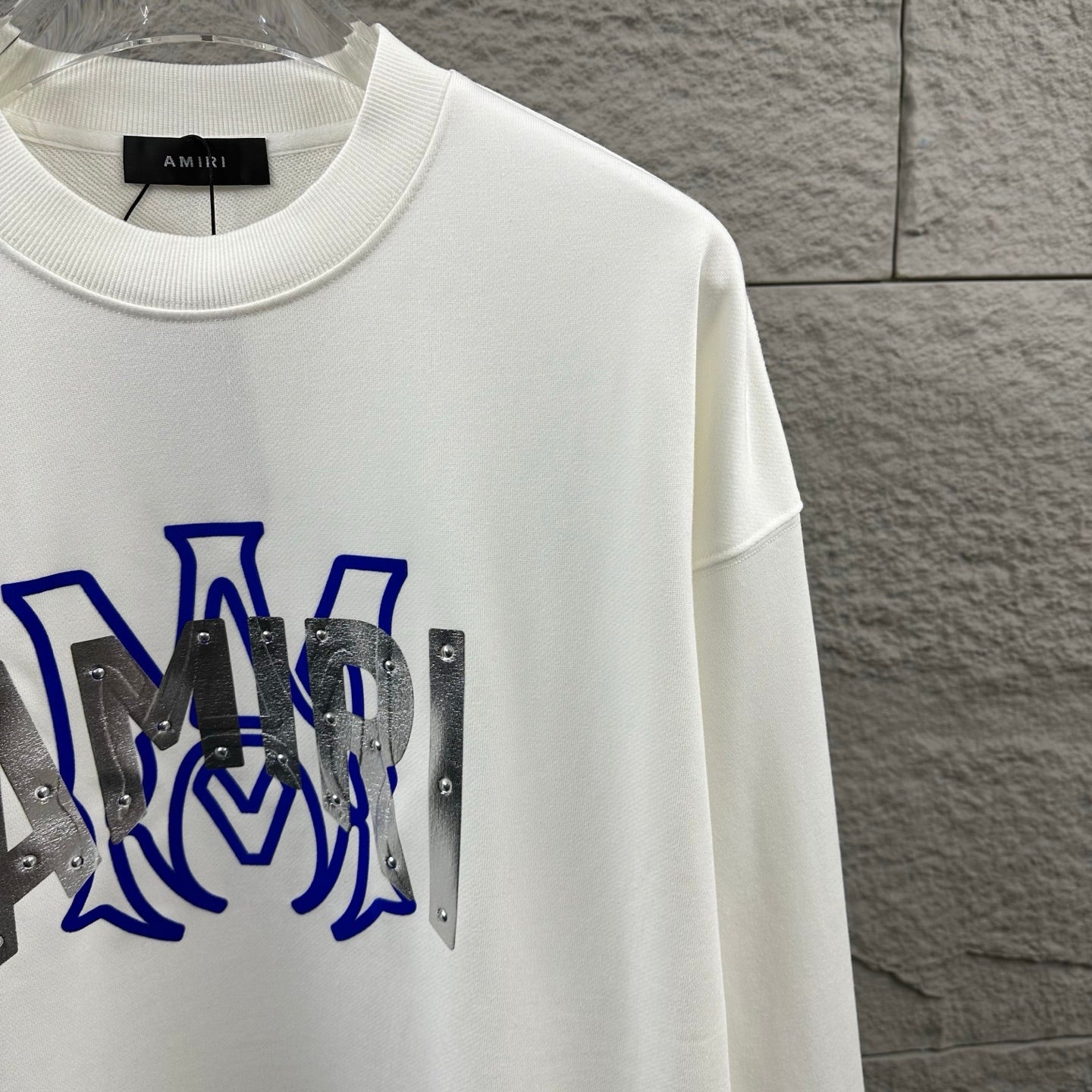 White Amiri crewneck sweatshirt close-up of blue graphic and silver metal panels