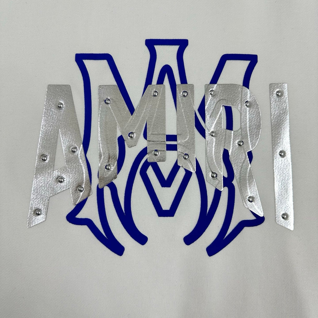 White Amiri sweatshirt graphic close-up showing blue letters and silver metal panels