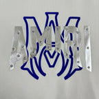 White Amiri sweatshirt graphic close-up showing blue letters and silver metal panels