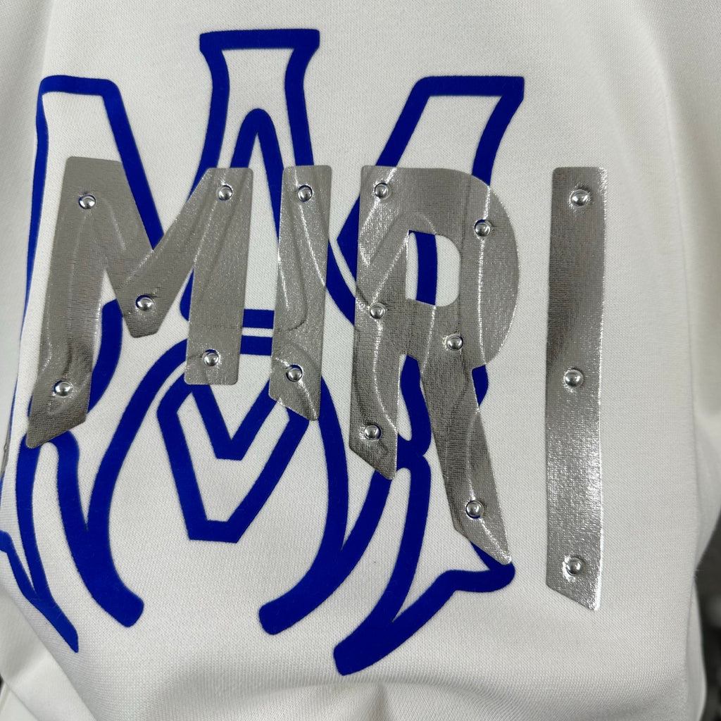 White Amiri sweatshirt graphic close-up with blue design and silver studded metal pieces