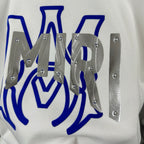 White Amiri sweatshirt graphic close-up with blue design and silver studded metal pieces