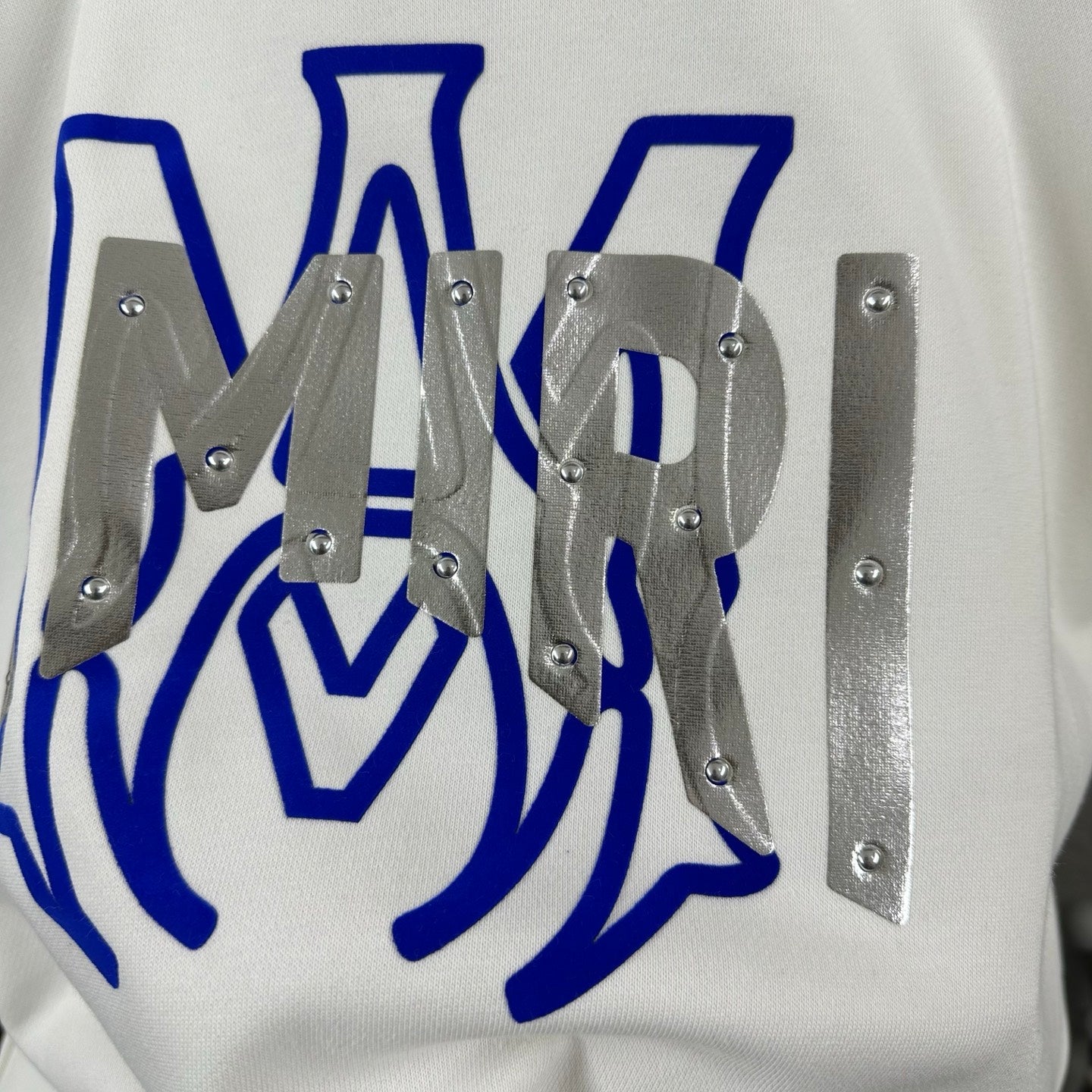 White Amiri sweatshirt graphic close-up with blue design and silver studded metal pieces