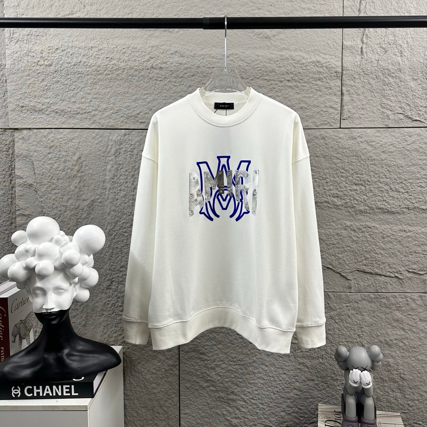 White Amiri crewneck sweatshirt with blue graphic lettering and silver metallic panels