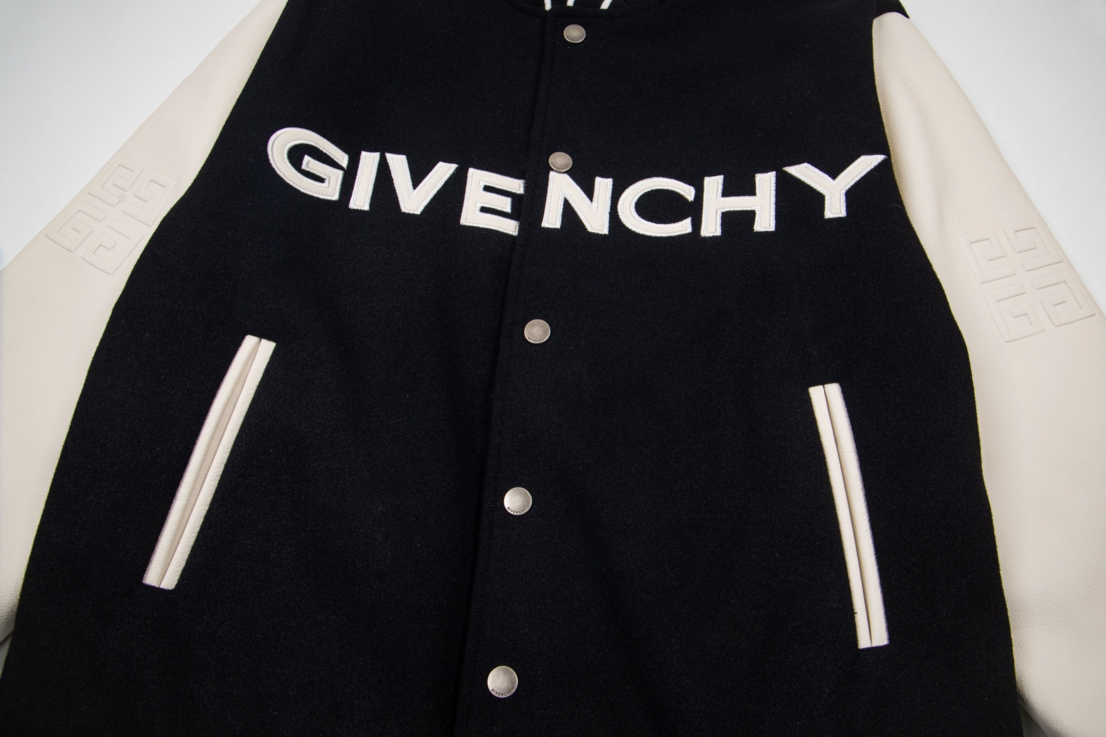 Black varsity jacket front with GIVENCHY logo, snap buttons, and striped ribbed cuffs