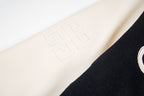 Cream sleeve detail with embossed geometric logo on black varsity jacket