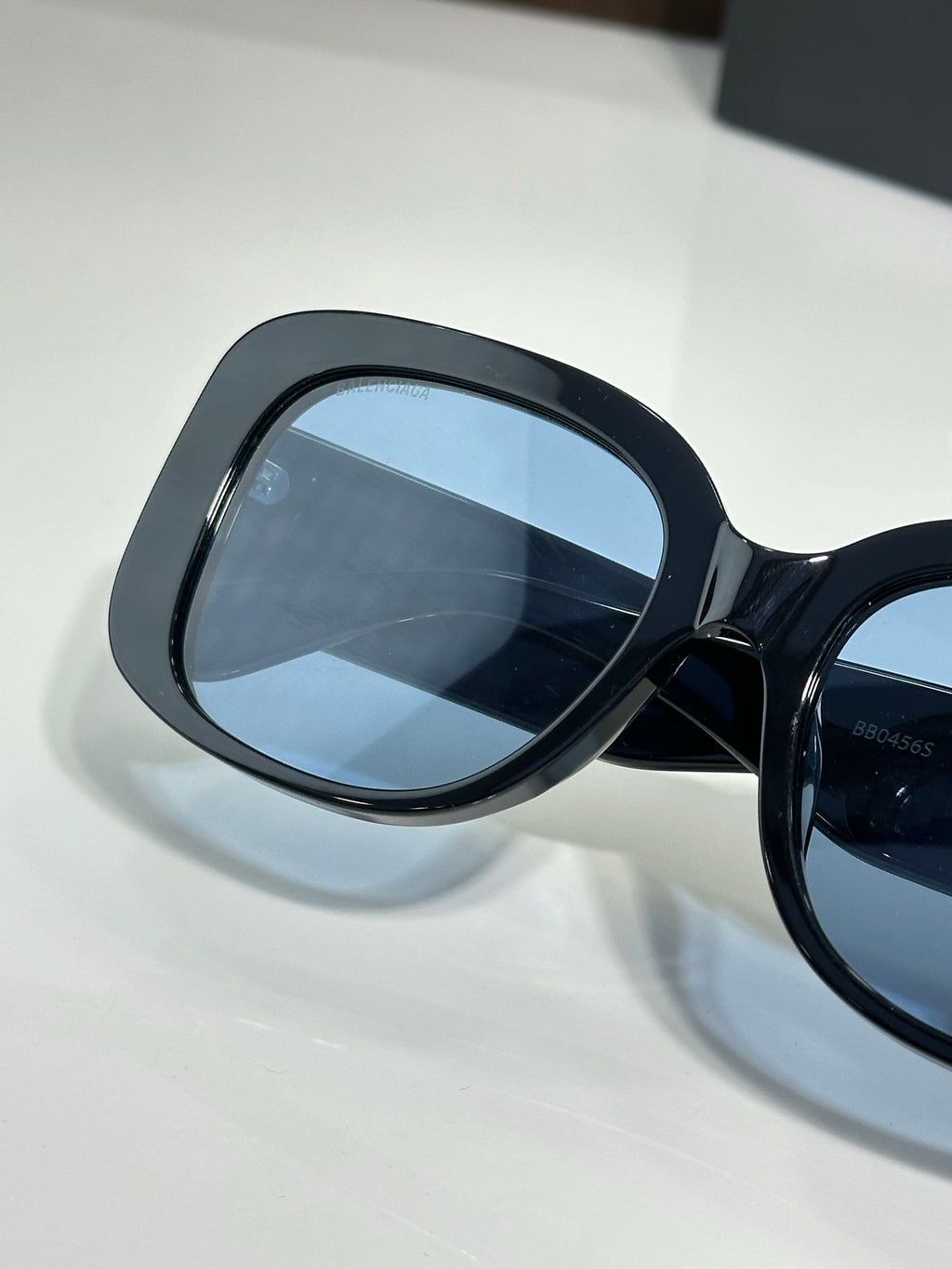 Sunglasses close-up with dark frame, blue lens, and BB logo arm detail
