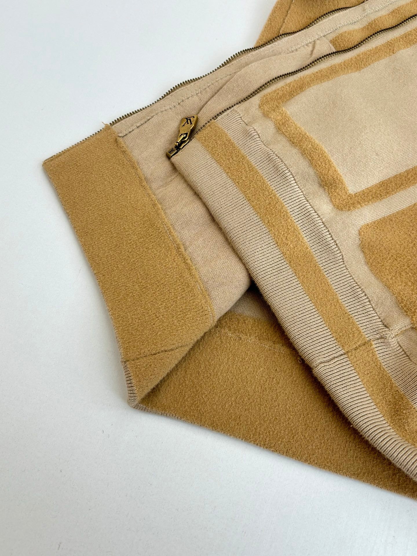 Beige knit jacket hem detail with zipper pull and gold trim