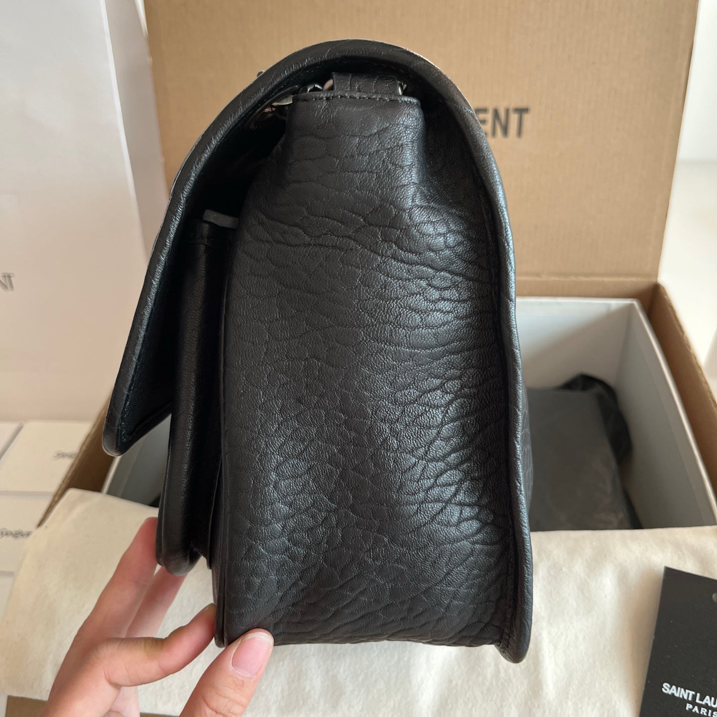 YSL bag side view with black textured leather and curved opening, smooth black lining