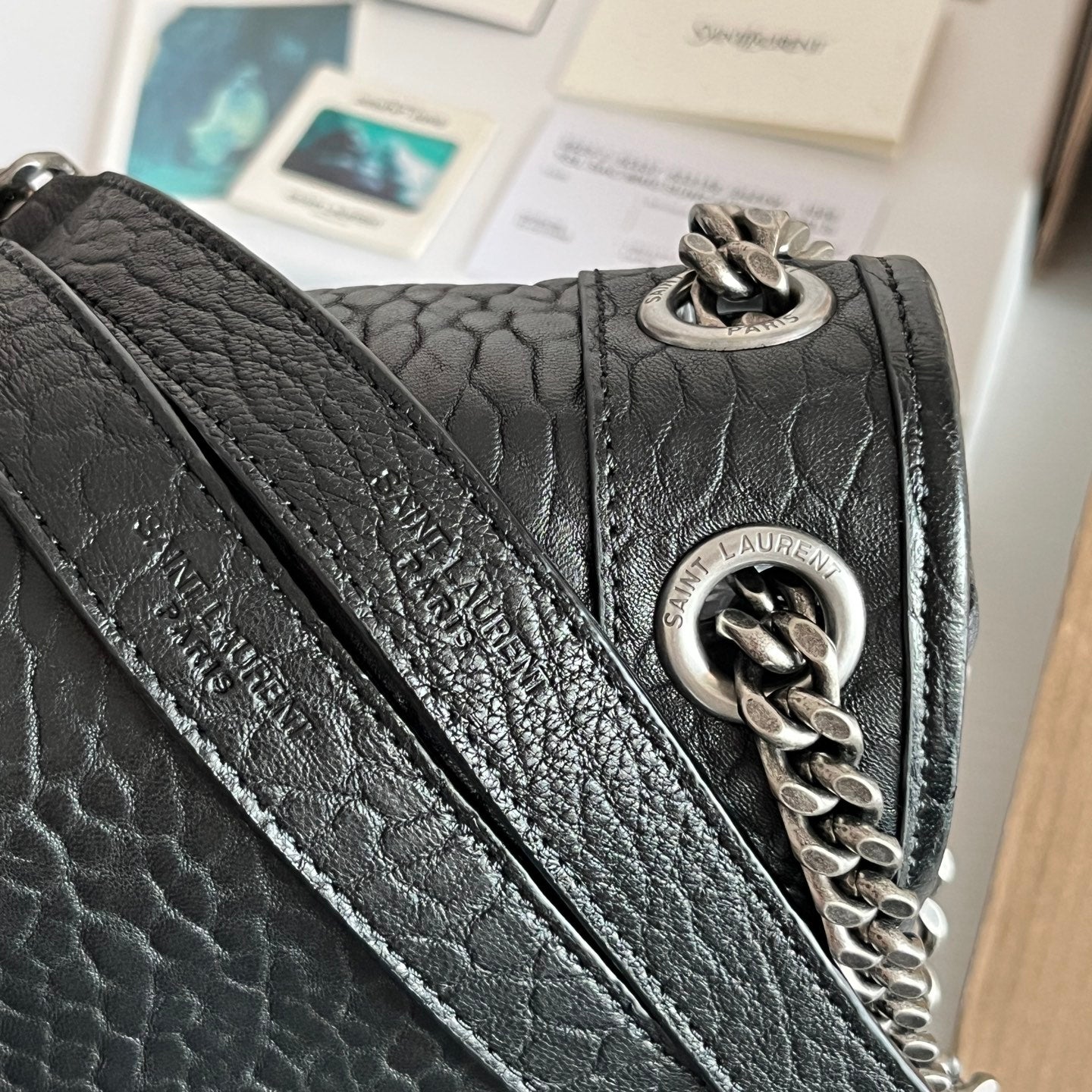 YSL bag clasp detail: silver chain and round emblem on black textured leather