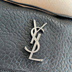 YSL bag front close-up: silver YSL monogram on black textured leather flap
