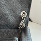 YSL bag corner close-up with silver chain links and round hardware on black leather