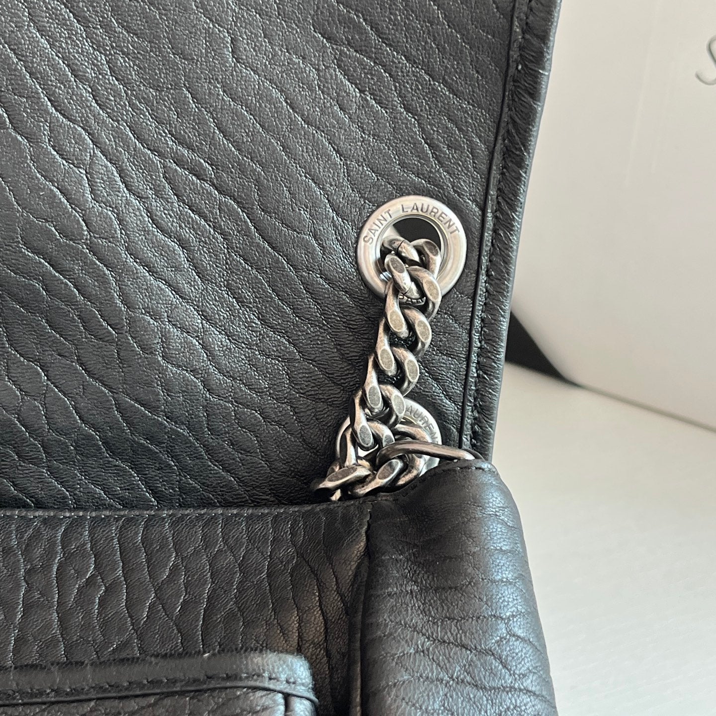 YSL bag corner close-up with silver chain links and round hardware on black leather