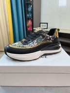 Black lace-up sneakers with gold-and-green patterned panels and thick white platform sole.