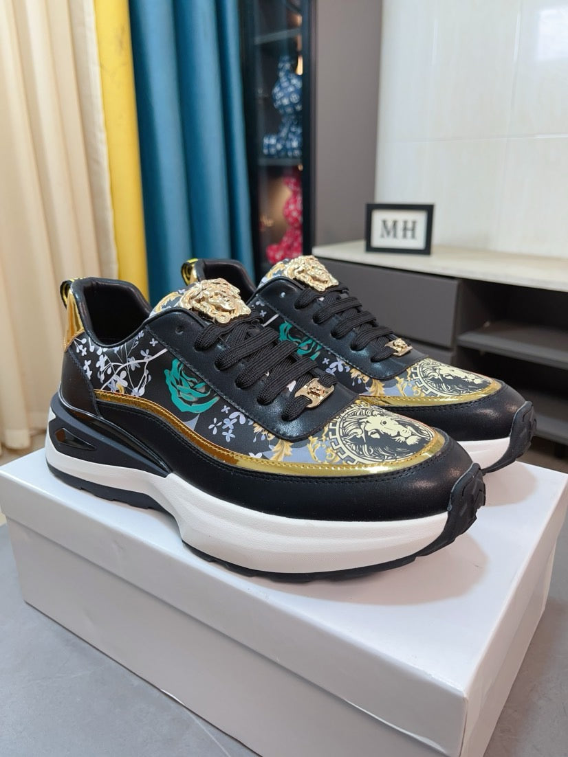 Black sneakers with gold edge trim, ornate graphic uppers, lace-up design and white sole.