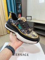 Black sneakers with ornate gold-and-green print, lace-up front, chunky white sole.