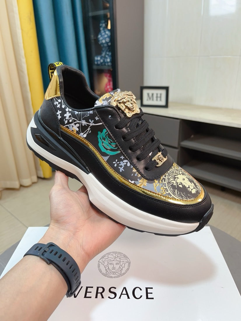 Black sneakers with ornate gold-and-green print, lace-up front, chunky white sole.