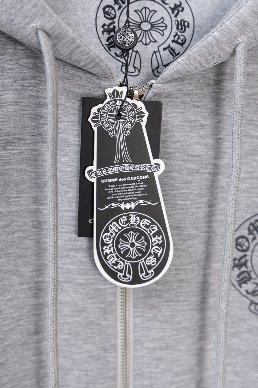 Grey zip hoodie with hanging tag labeled Comme des Garçons.