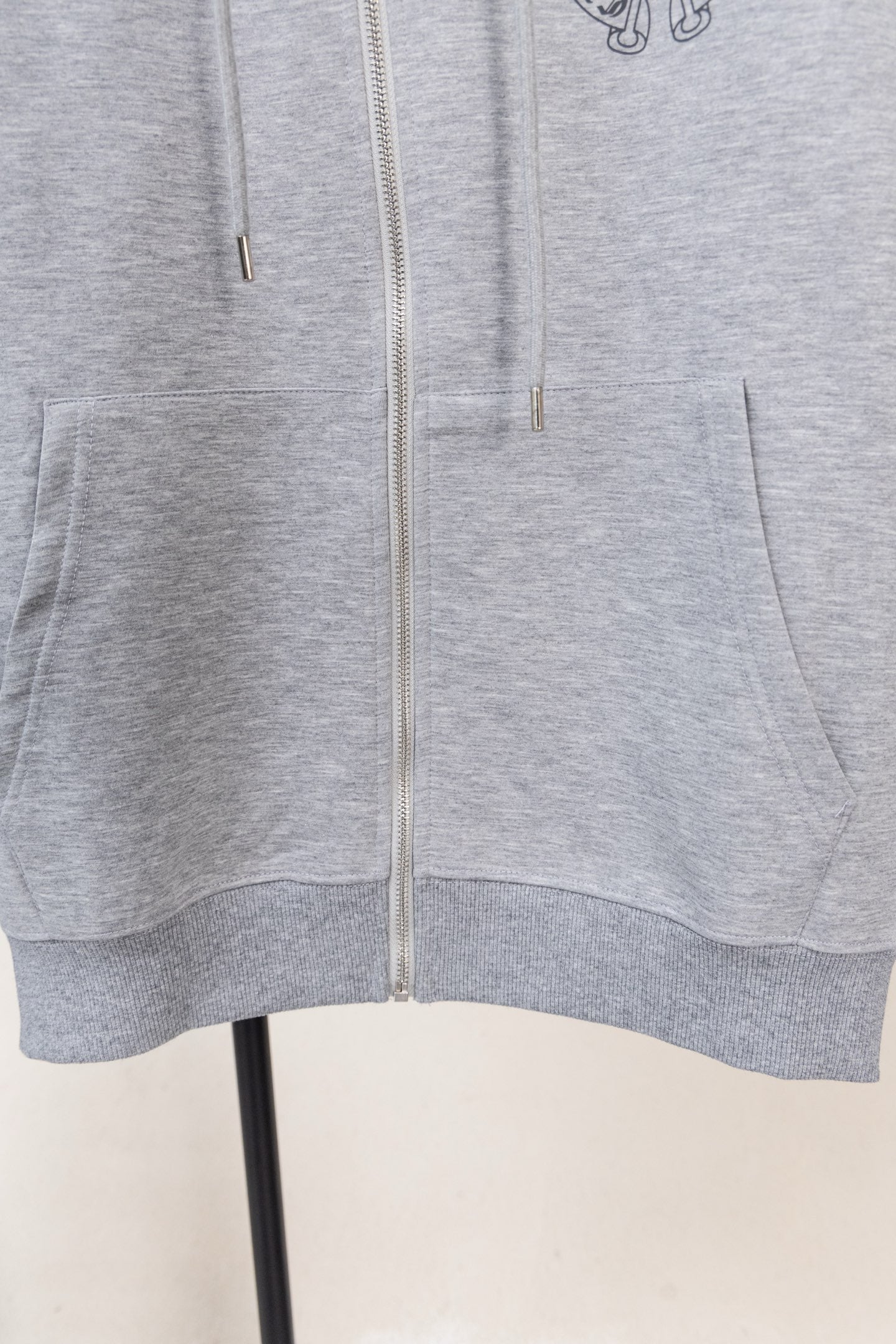 Grey zip hoodie hem with front pocket openings and centered zipper.