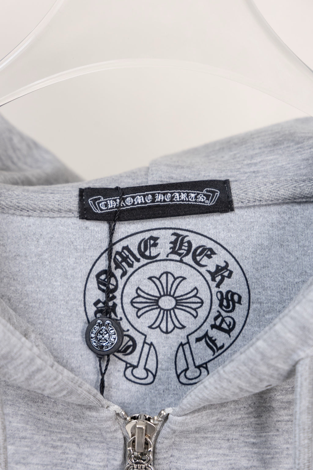 Grey hoodie collar with printed logo label and central zipper pull.