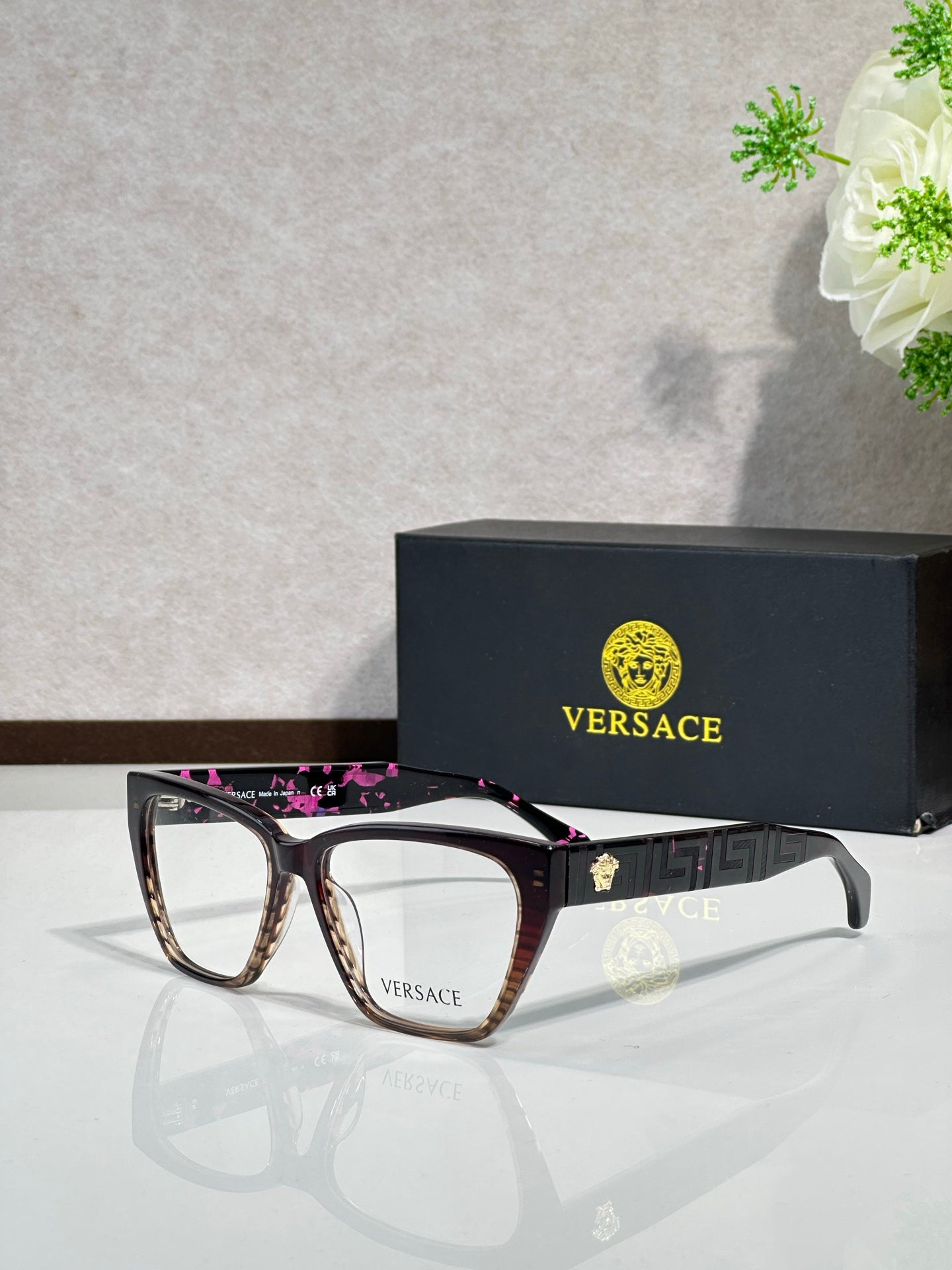 Black rectangular eyeglasses with pink patterned temple accents and VERSACE logo