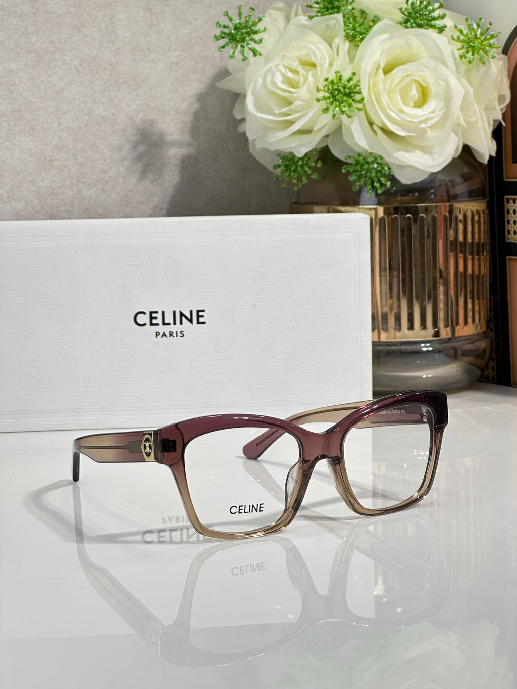 Burgundy and tan eyeglass frames with clear lenses and gold-tone front logo