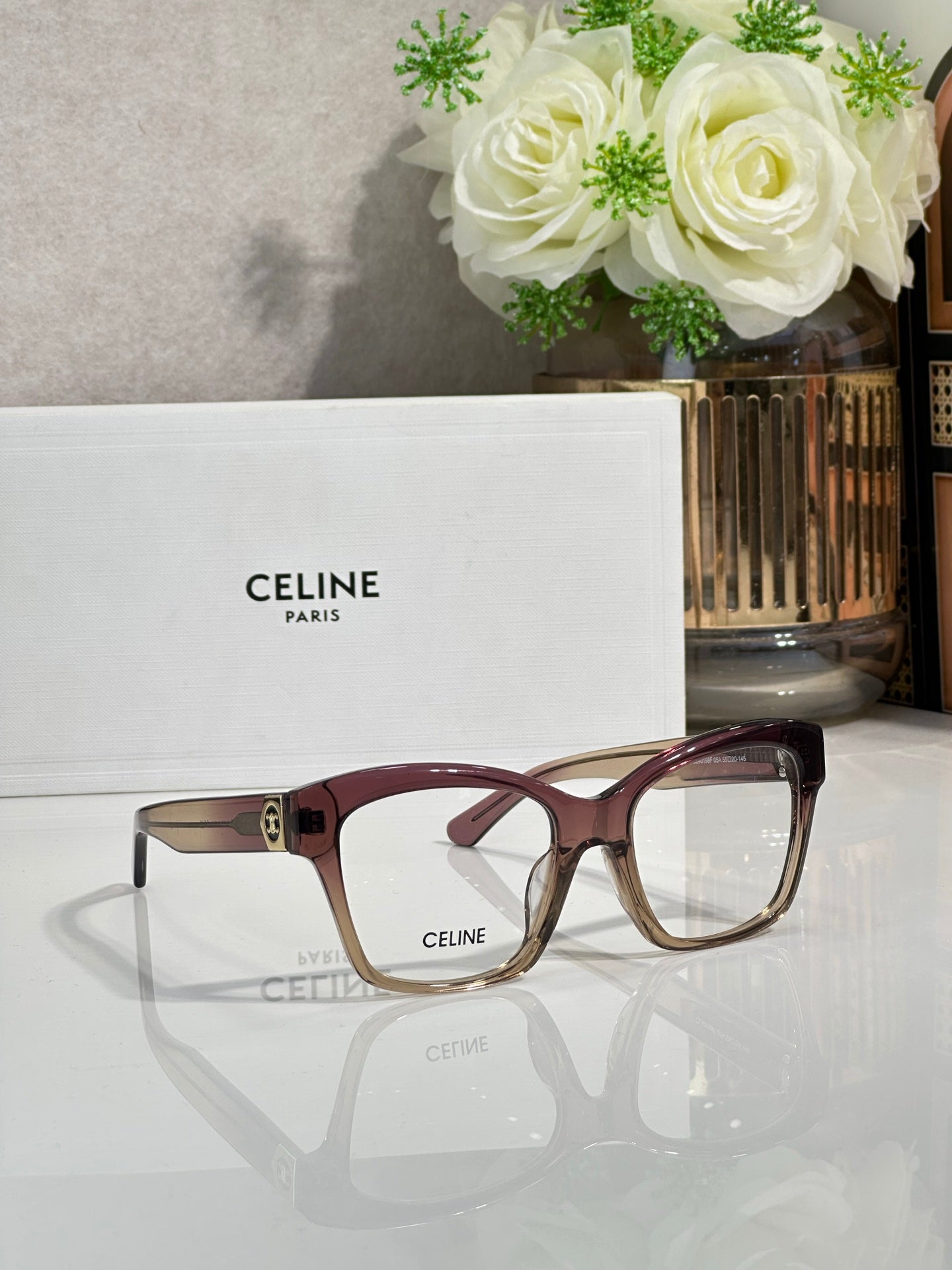 Burgundy and tan eyeglass frames with clear lenses and gold-tone front logo