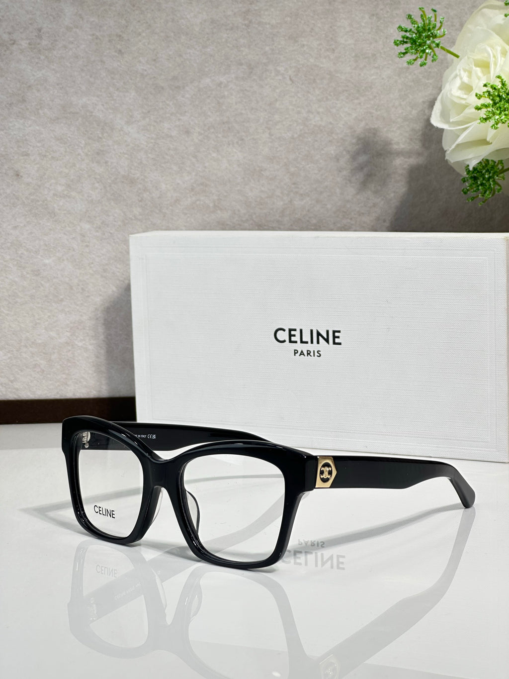 Black squared eyeglass frames with clear lenses and gold-tone logo at temple