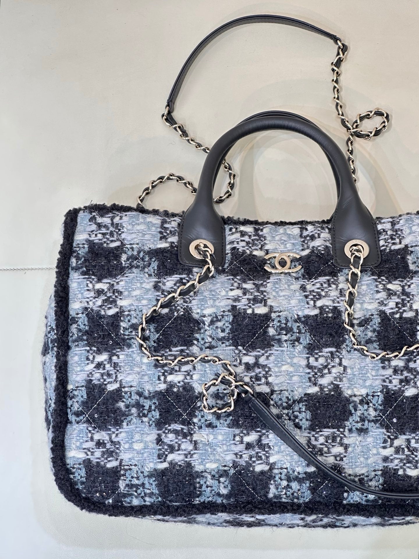 Chanel tote bag with blue/black/white tweed pattern, black handles, and chain shoulder strap