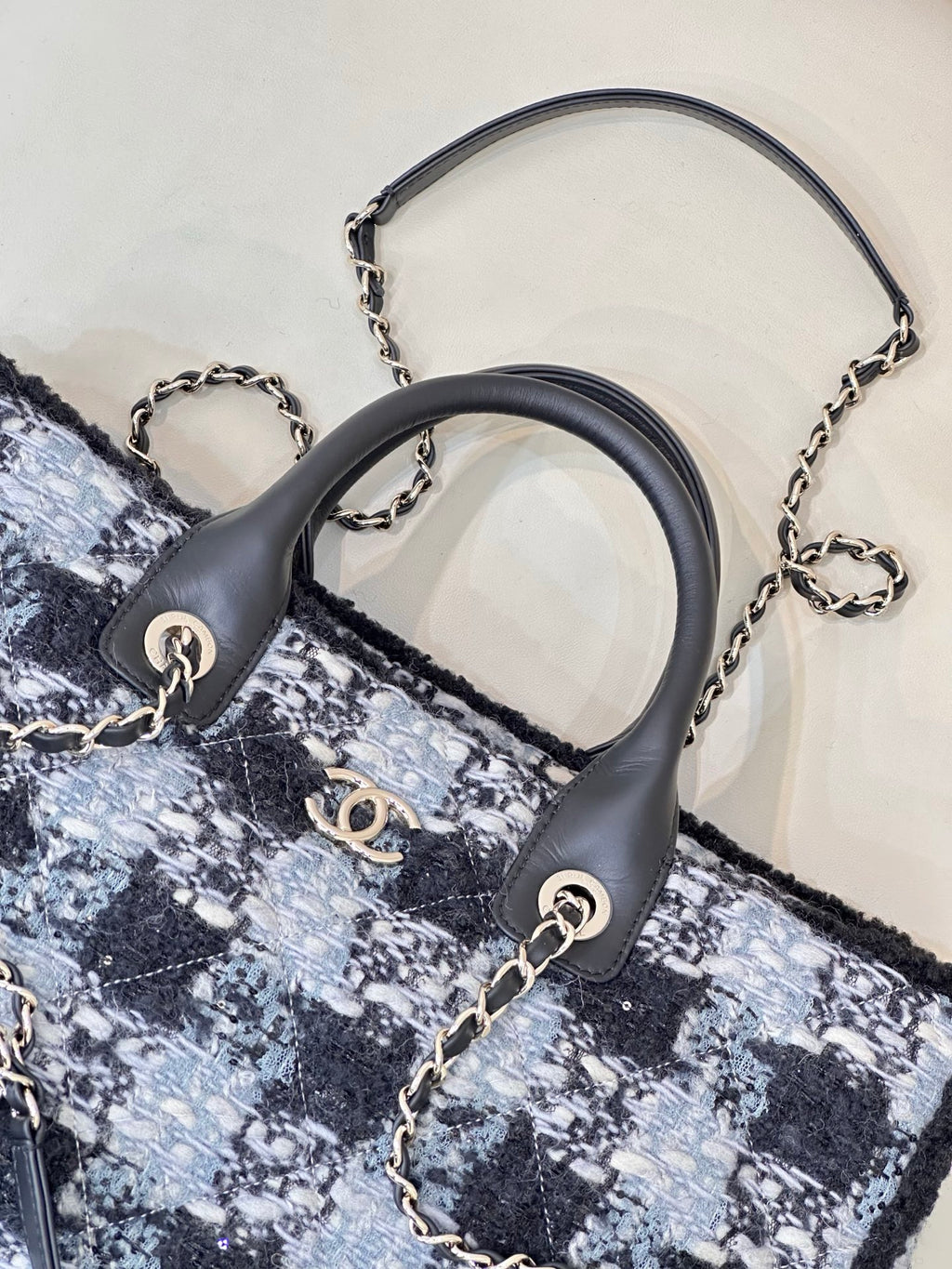 Chanel tote bag close-up: black leather handles with chain accents on blue tweed