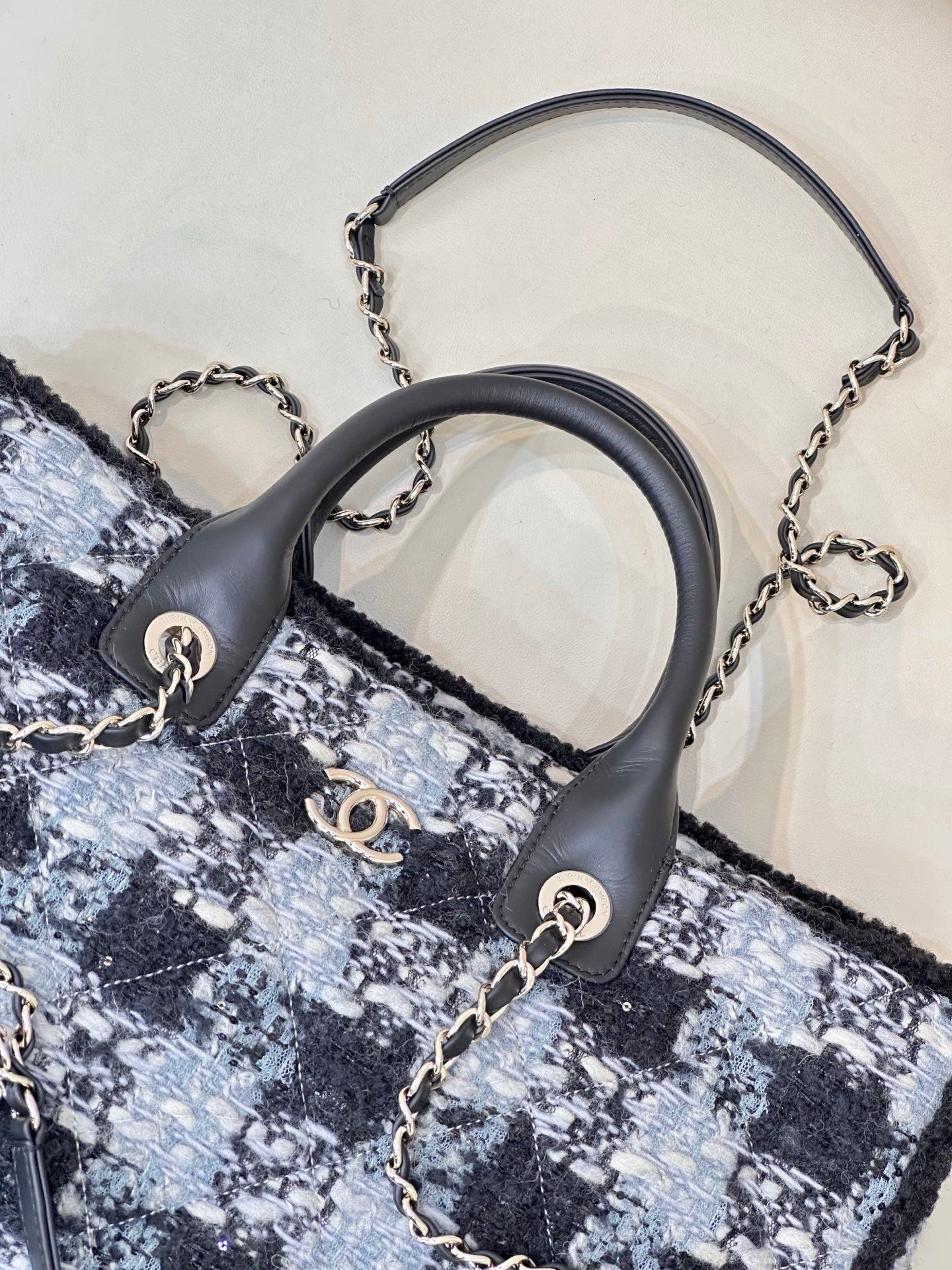 Chanel tote bag close-up: black leather handles with chain accents on blue tweed
