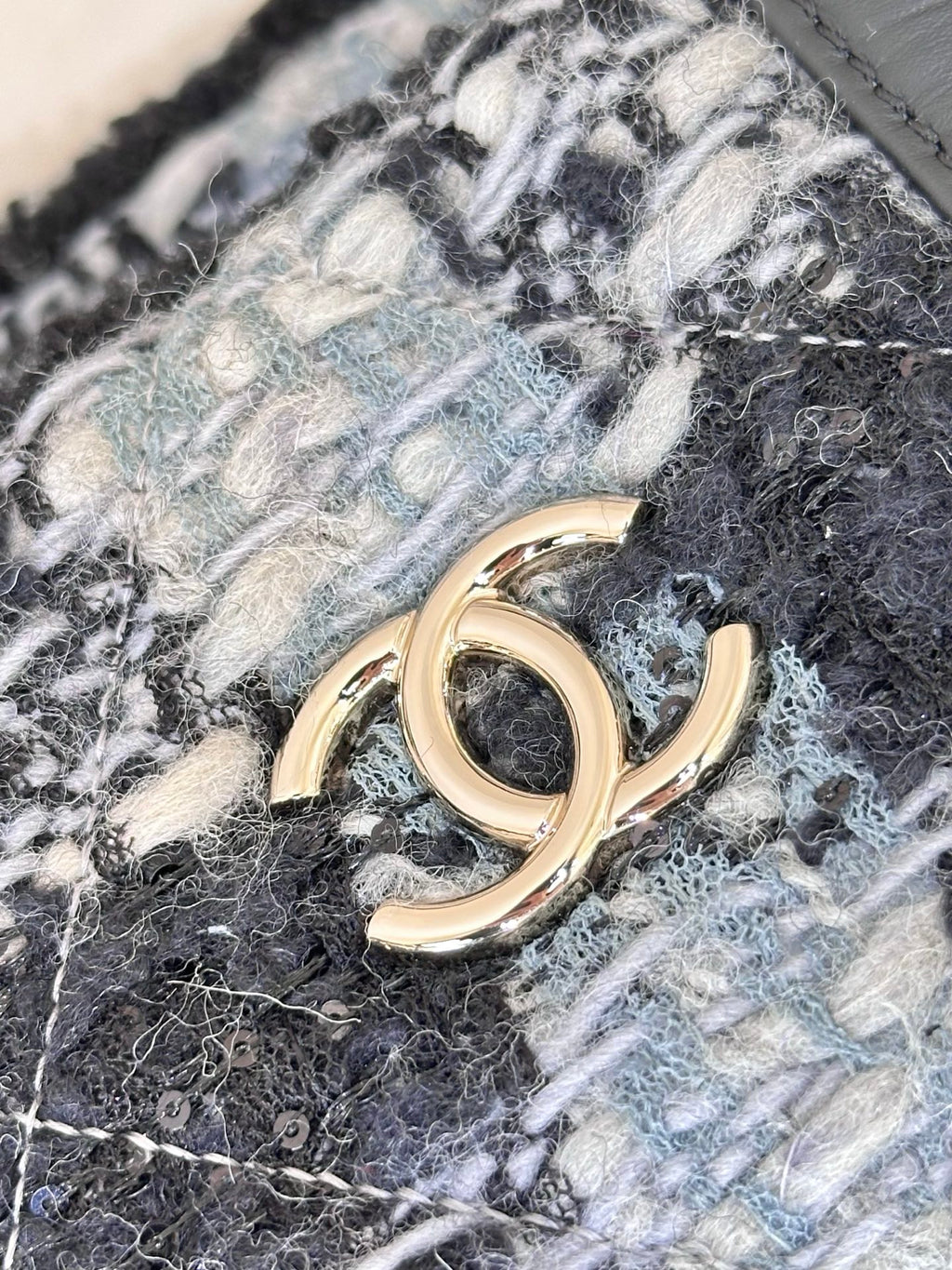 Chanel tote bag detail: gold-tone CC-style logo on blue and black tweed