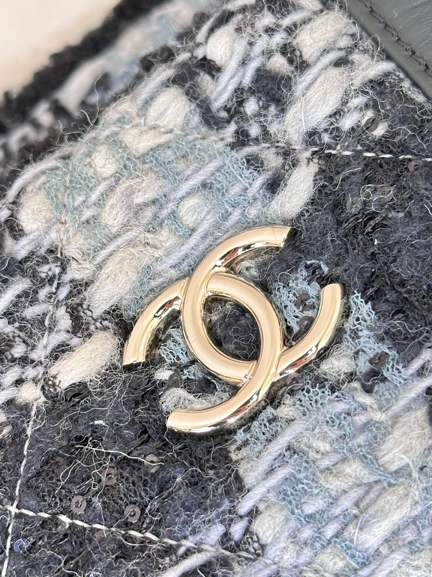 Chanel tote bag detail: gold-tone CC-style logo on blue and black tweed