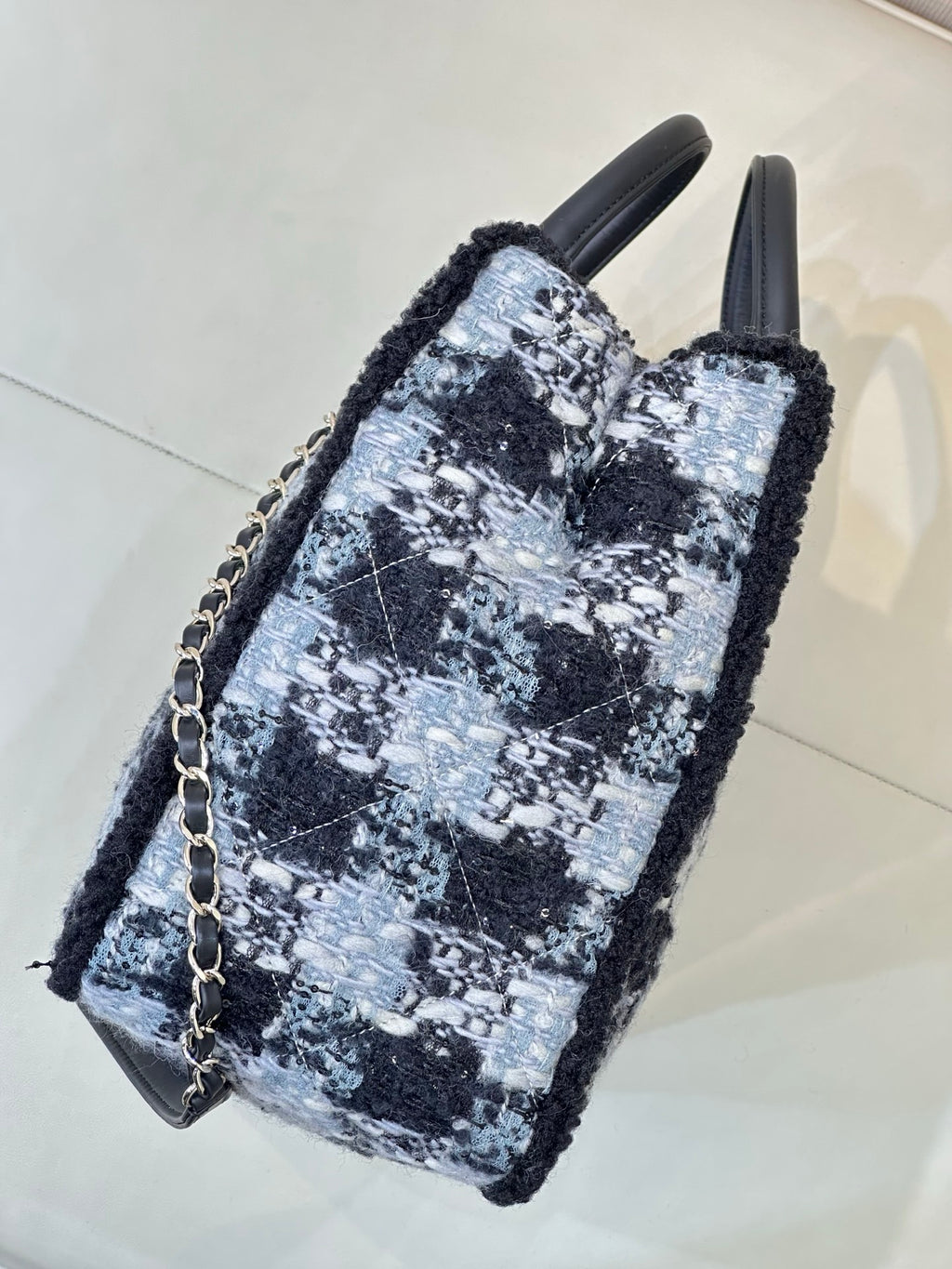 Chanel tote bag side view in blue/black tweed with black leather base and chain strap