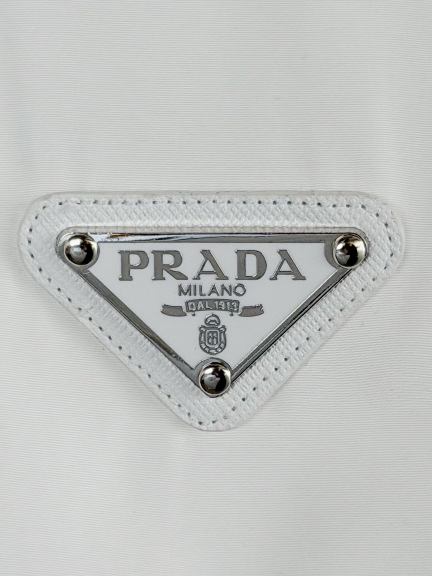 Triangular Prada Milano logo patch with silver studs on white T-shirt